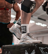 Load image into Gallery viewer, A guy performing a double dumbbell box over wearing the amazing DFNT. performance socks.  As demonstrated, these socks are designed to stay put in the most vigorous of workouts with their perfect fit and elasticated top. The socks pictured are white with a black box incasing a negative space DFNT. logo.