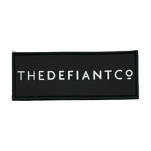 Load image into Gallery viewer, A photo of a velcro patch designed to stick to your gym bag.  The finish is rubber. the main colour is black and the text is white.  The patch states The Defiant Co.