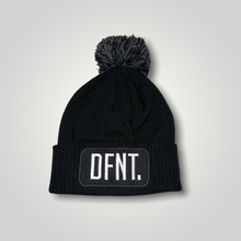Load image into Gallery viewer, A black beanie hat with a two tone black and white bobble on top. The hat is branded with DFNT. embroidered on the centre patch in white. It is soft to the touch and has a double layer knit and ribbed cuff.