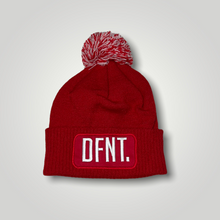 Load image into Gallery viewer, A red beanie hat with a two tone red and white bobble on top. The hat is branded with DFNT. embroidered on the centre patch in white. It is soft to the touch and has a double layer knit and ribbed cuff.