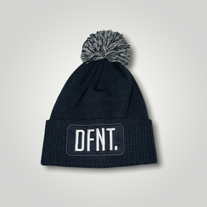 A navy blue beanie hat with a two tone navy and white bobble on top. The hat is branded with DFNT. embroidered on the centre patch in white. It is soft to the touch and has a double layer knit and ribbed cuff.