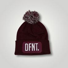 Load image into Gallery viewer, A burgundy beanie hat with a two tone burgundy and white bobble on top. The hat is branded with DFNT. embroidered on the centre patch in white. It is soft to the touch and has a double layer knit and ribbed cuff.