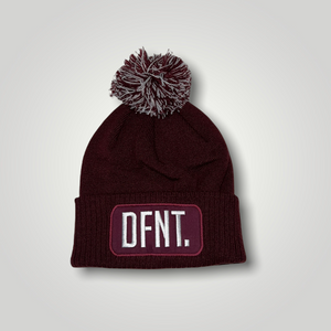 A burgundy beanie hat with a two tone burgundy and white bobble on top. The hat is branded with DFNT. embroidered on the centre patch in white. It is soft to the touch and has a double layer knit and ribbed cuff.